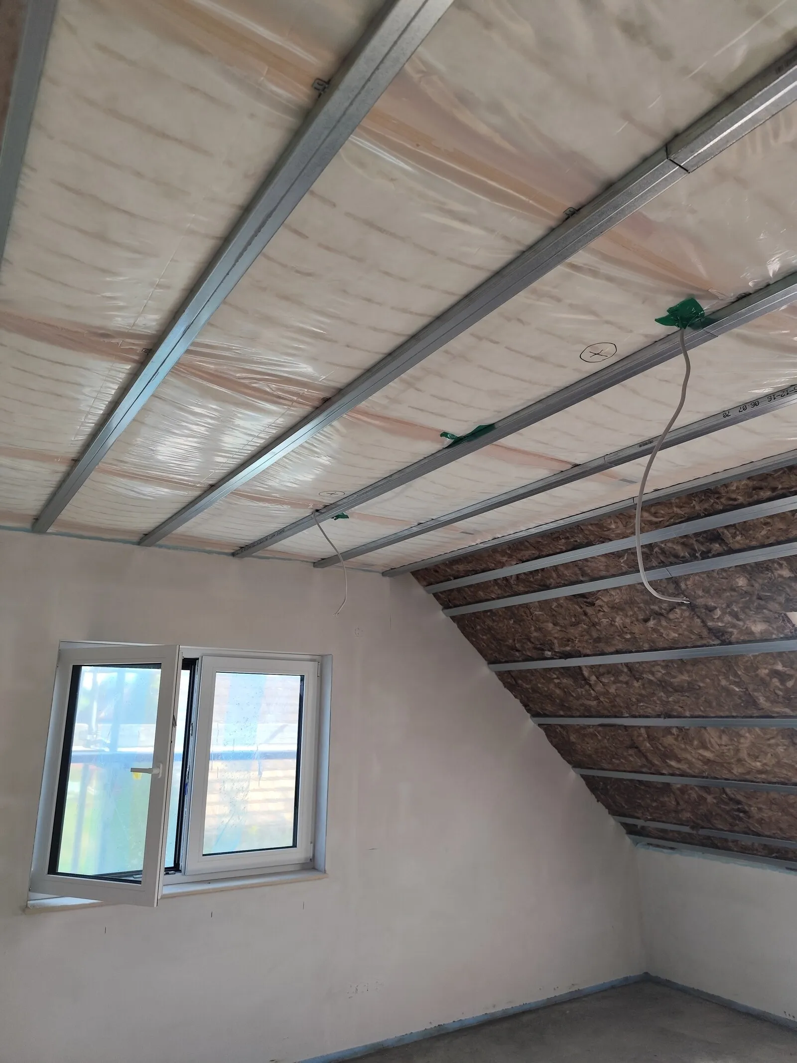 Dachgeschoss im Trockenbau-Ausbau: Metall-Unterkonstruktion an der Decke mit Dampfsperre und Dämmung, Fenster in der Giebelwand, vor der Beplankung.